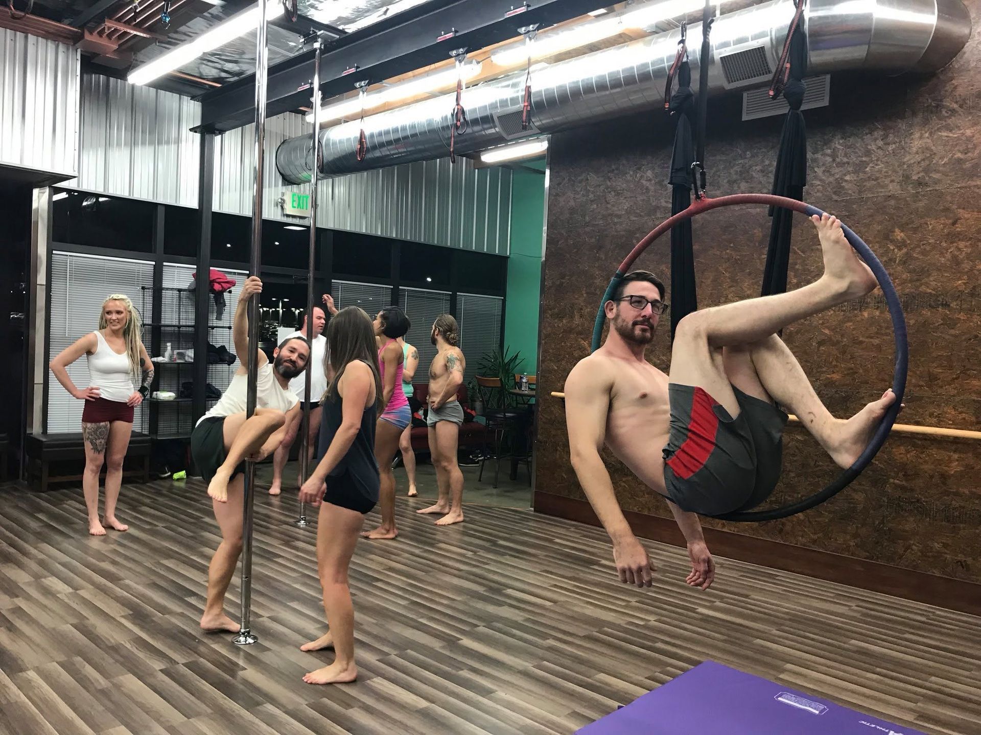 People practicing aerial hoop in a studio, with one man hanging in a hoop and others nearby.