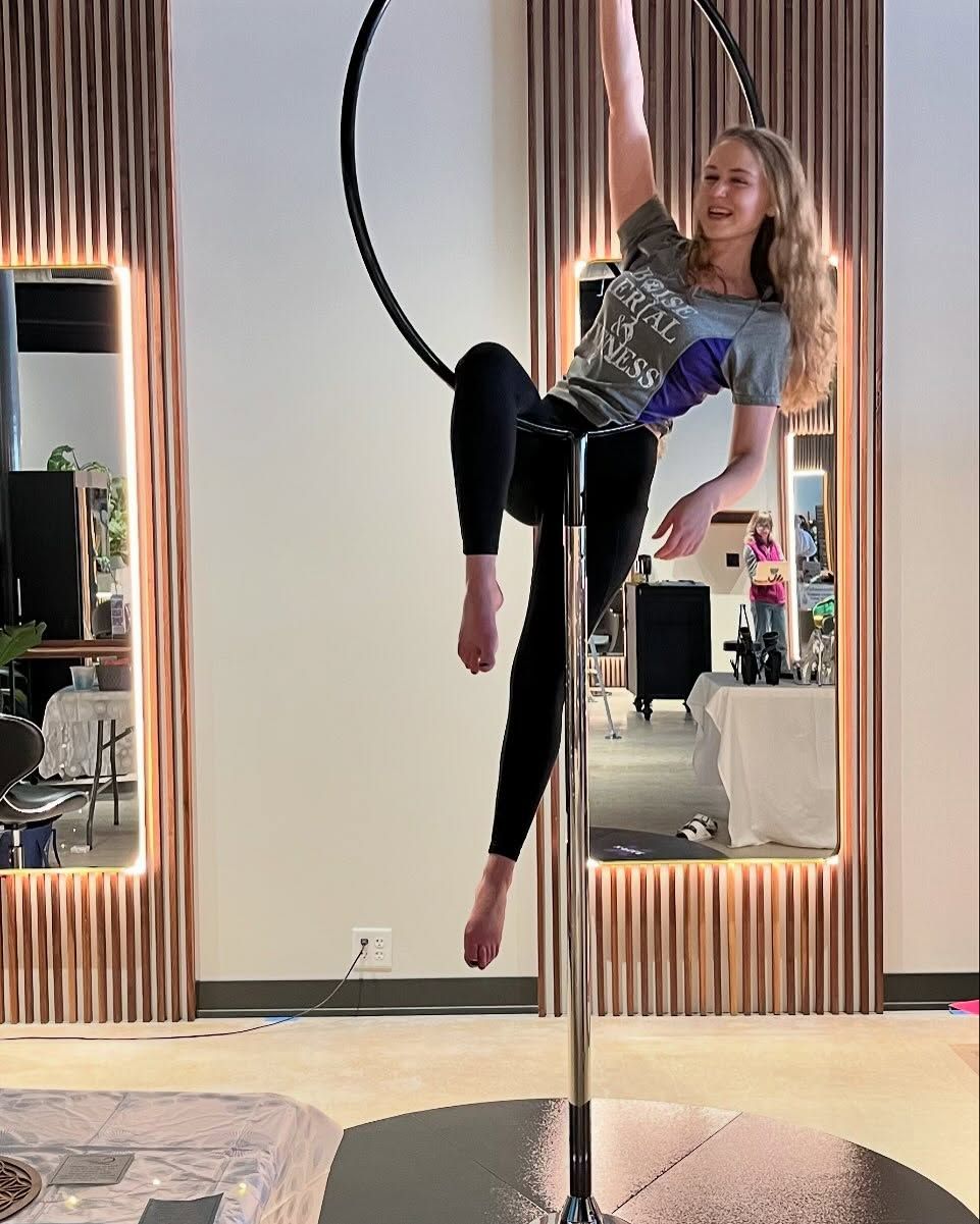 Woman hanging from a hoop in a studio, wearing black leggings and a patterned top.