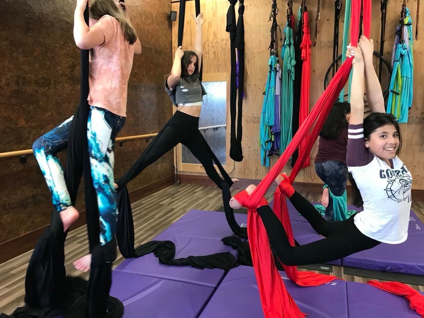 People doing aerial yoga with red and black hammocks in a studio on purple mats