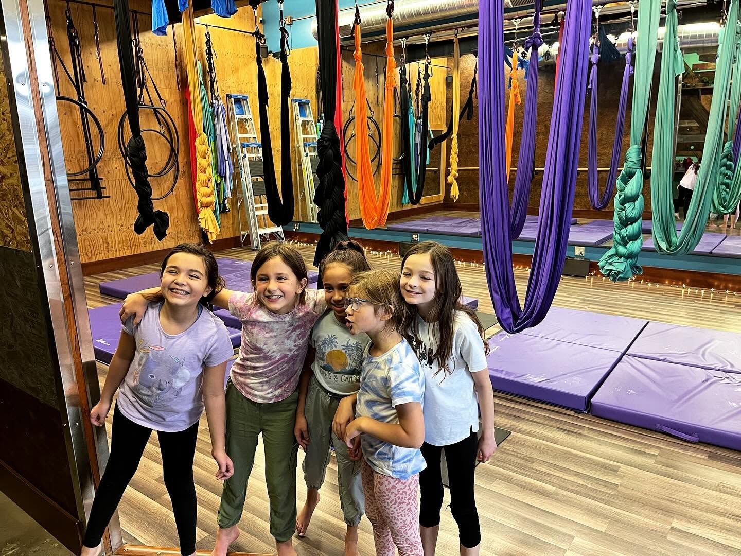 Four children posing in a gymnastics studio with colorful hanging ropes and purple mats