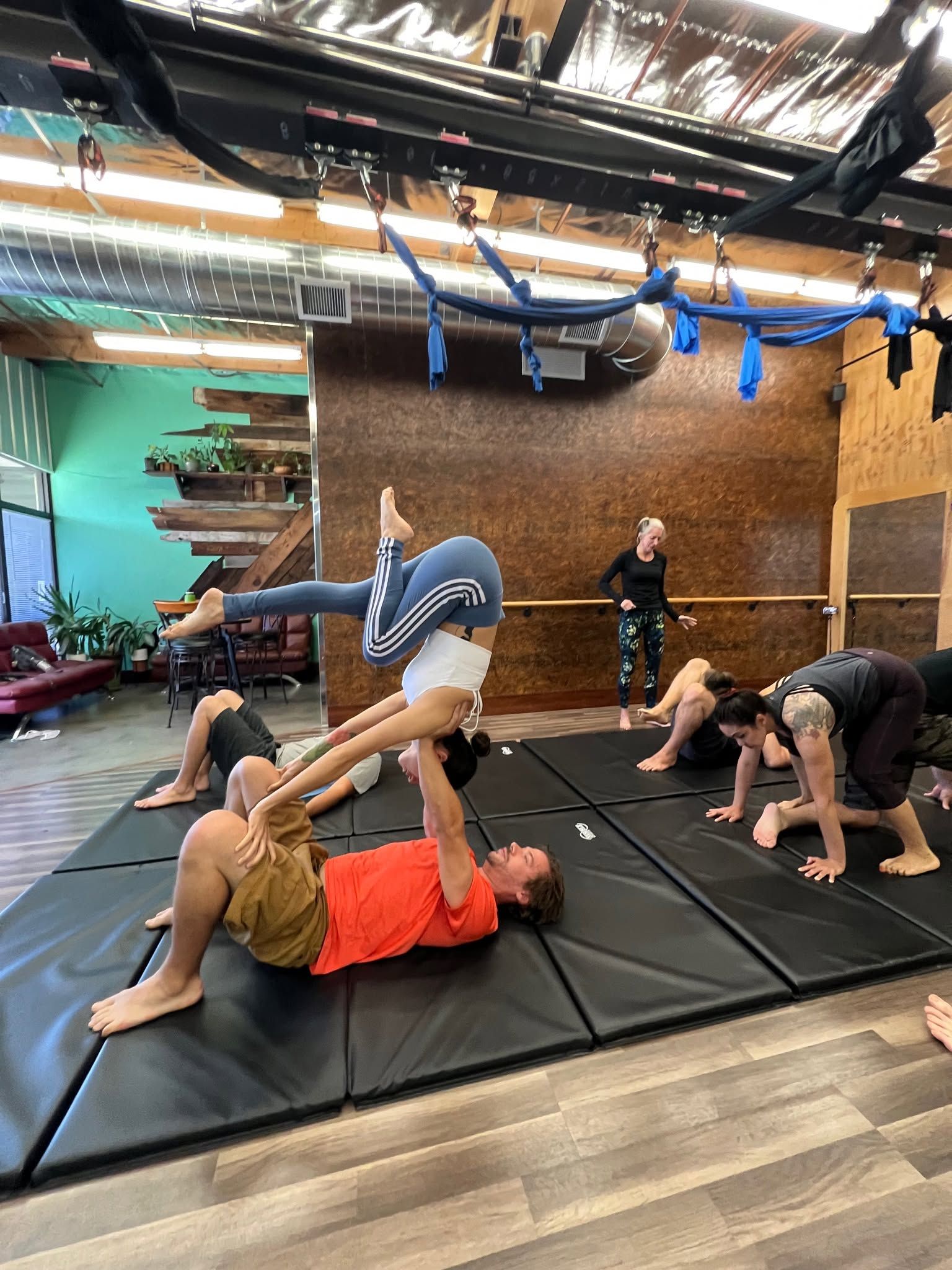 People doing partner acrobatics and stretching on mats in a studio with hanging blue straps