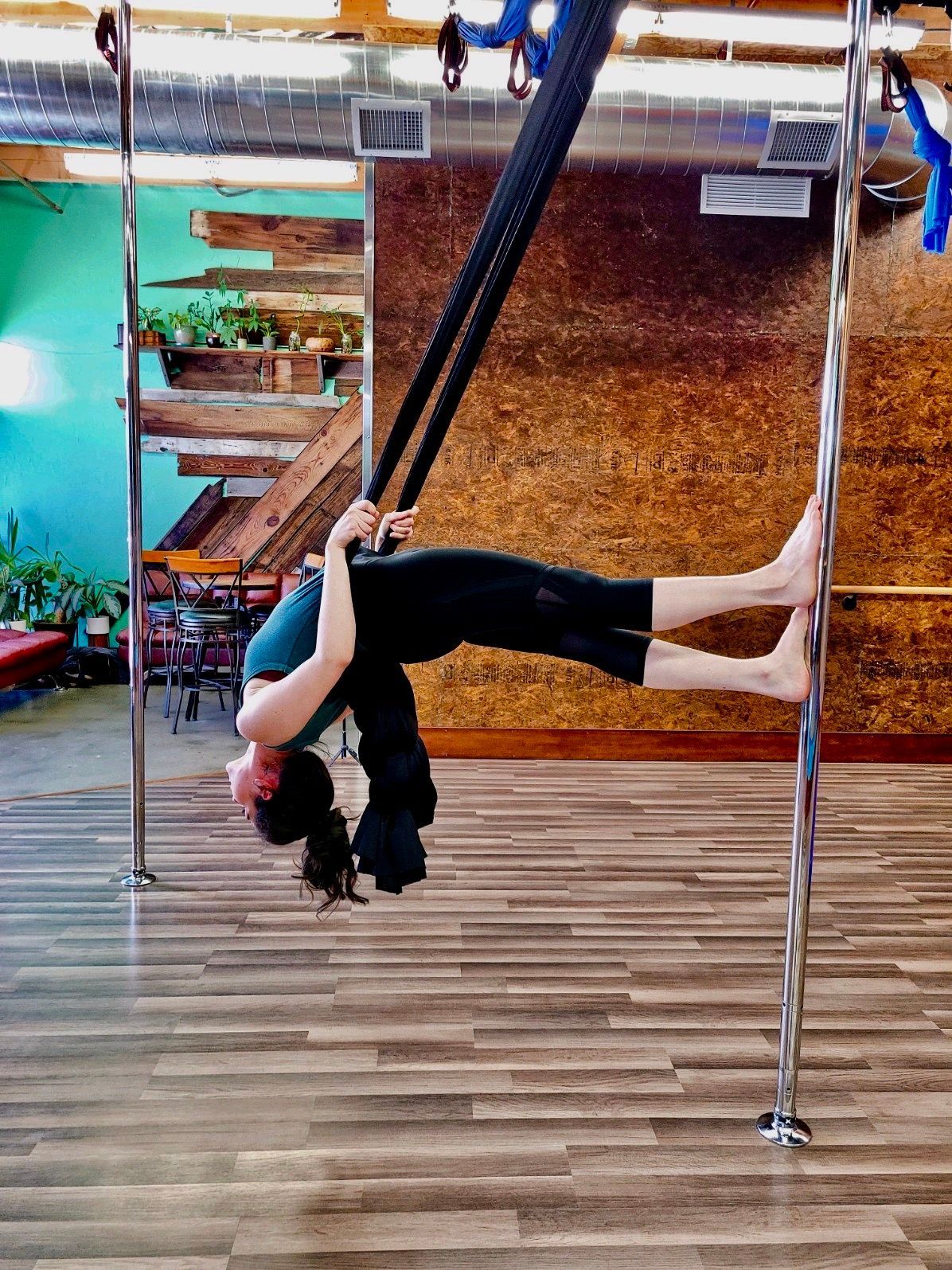Woman doing an aerial backbend on a pole in a studio with wooden floor and turquoise walls
