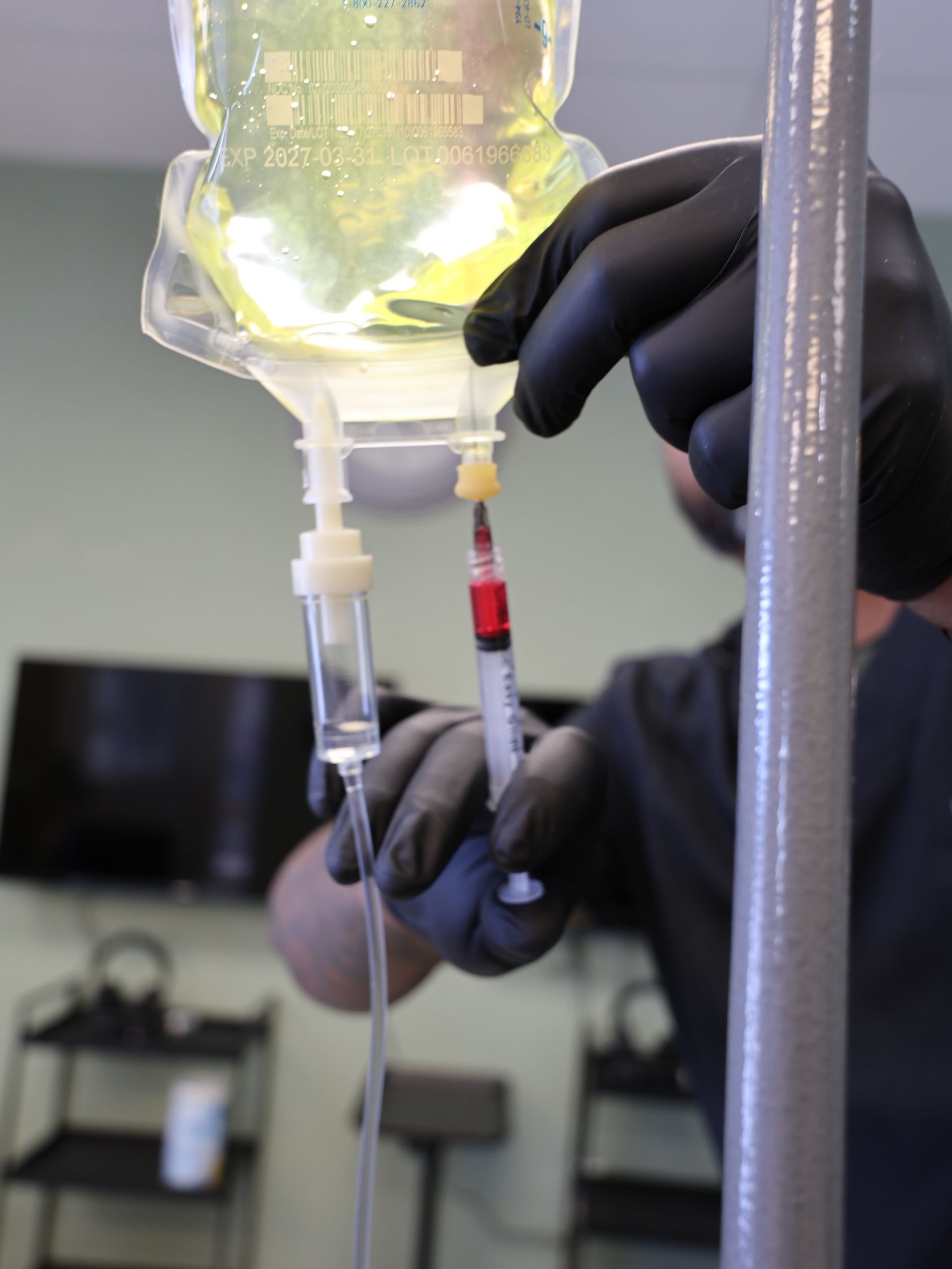 Person in black gloves drawing liquid from IV bag with a syringe. Level Up Falcon