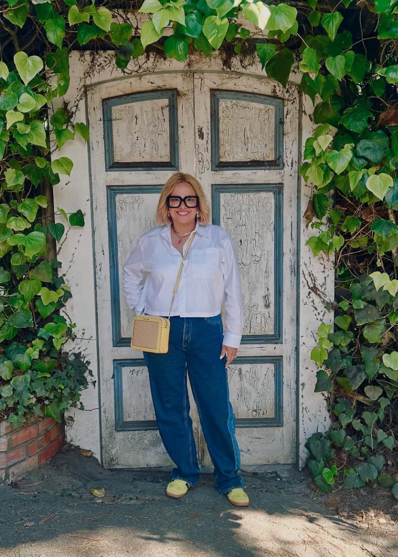 Woman in white shirt and jeans poses in front of a weathered white door, ivy surrounding. Level Up Falcon