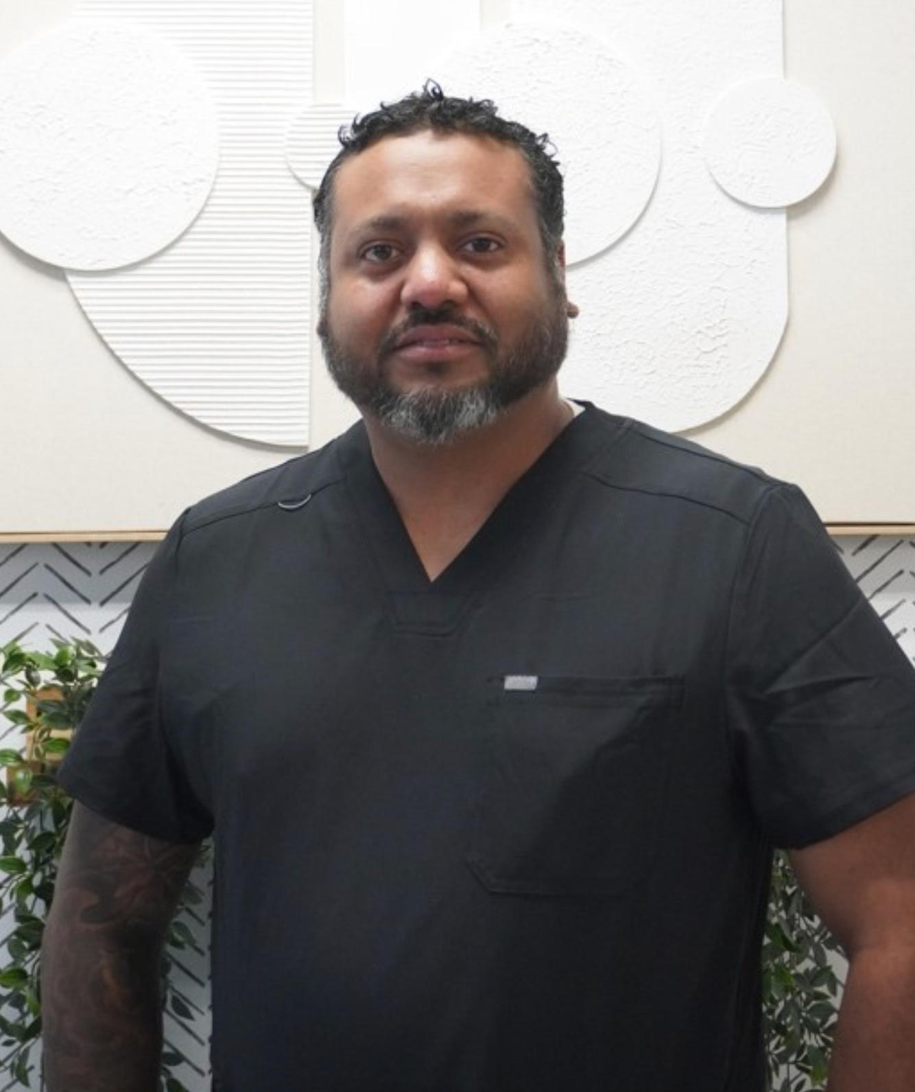 Man in black scrubs, looking at the camera. Neutral background, possibly in a medical office. Level Up Falcon