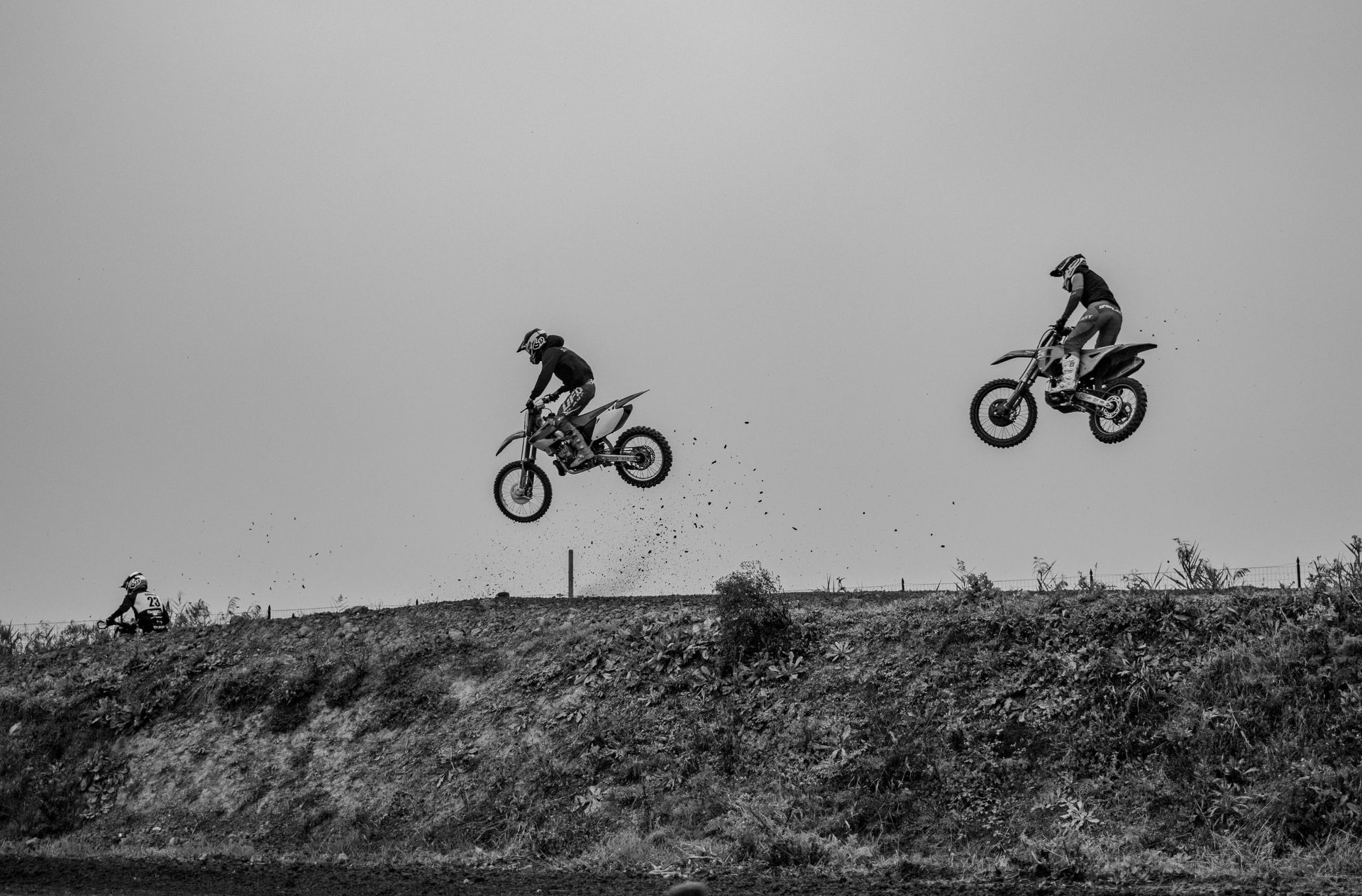 Two dirt bikes in mid-air over a dirt mound, rider silhouettes against a bright sky. Level Up Falcon