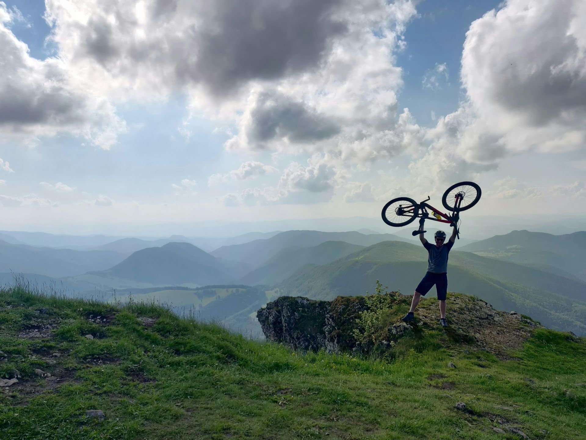 Person holding a mountain bike over their head on a mountaintop. Level Up Falcon