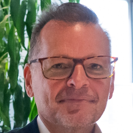 A man in a suit and white shirt is smiling for the camera.