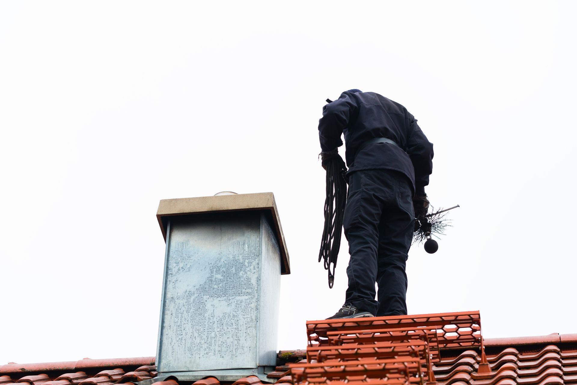 A man is standing on top of a chimney on a roof.