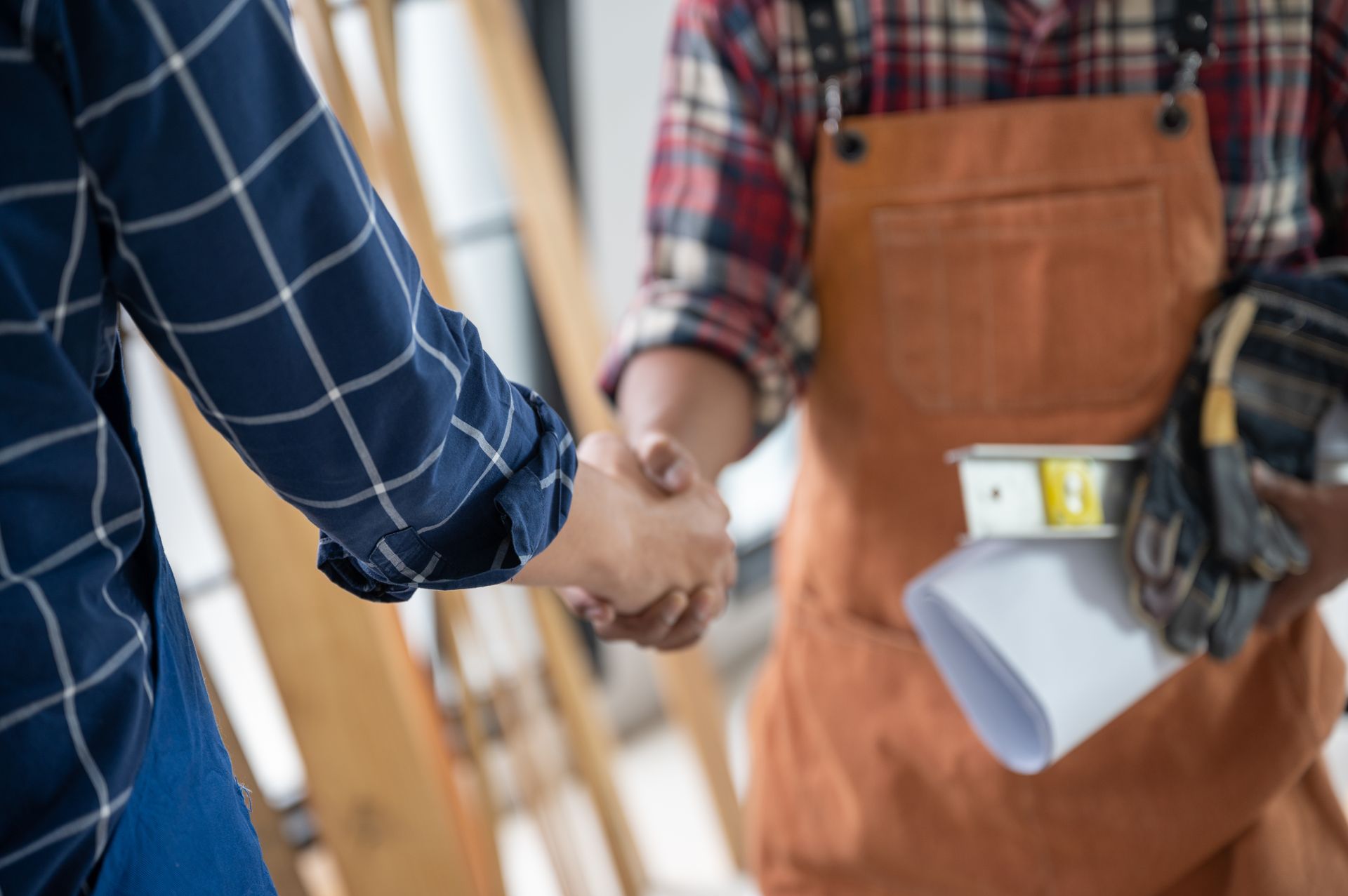 A man is shaking hands with a construction worker while holding a blueprint.