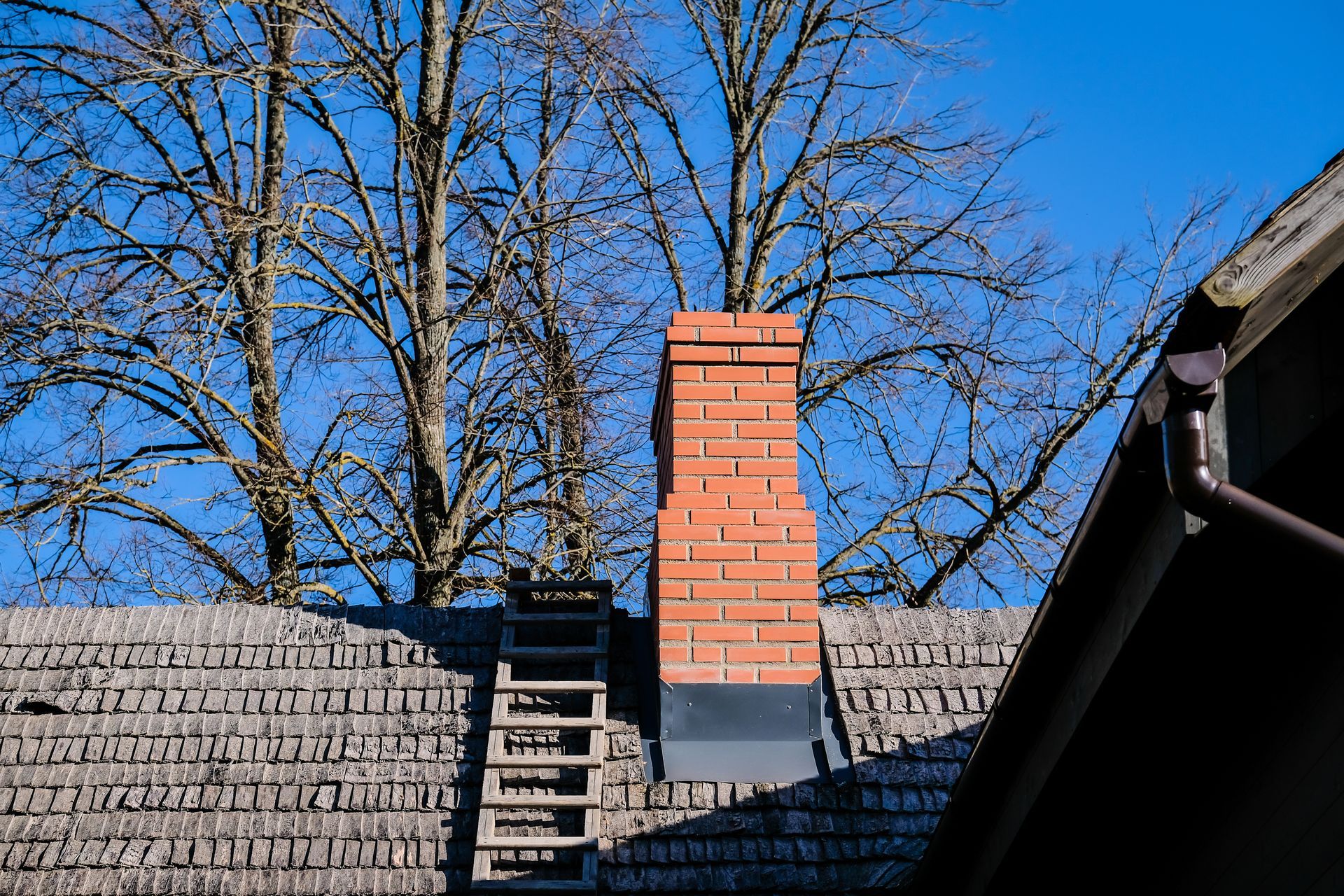 A brick chimney on the roof of a house with a ladder attached to it.
