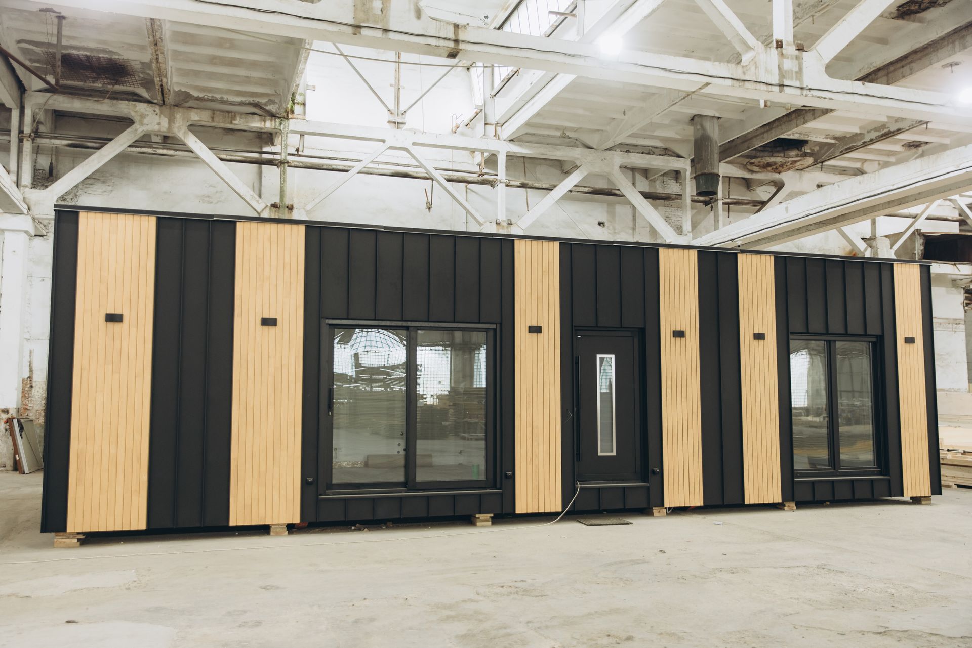 A black and wooden building with a lot of windows is sitting in a warehouse.