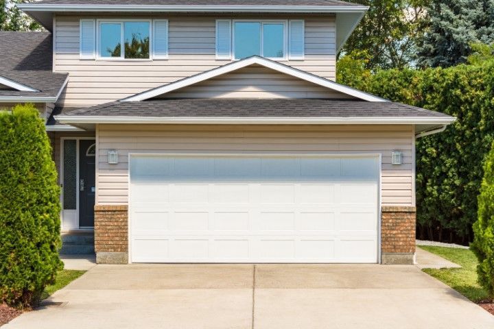 Suburban house exterior with white garage door, beige siding, and concrete driveway