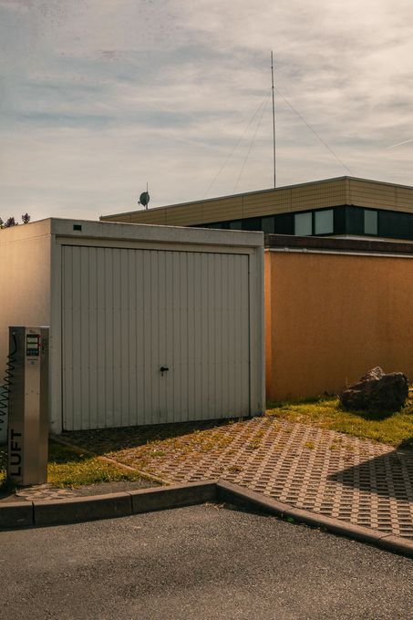 White garage doors beside a tan house, with a gravel driveway and a small grassy patch under a cloudy sky.