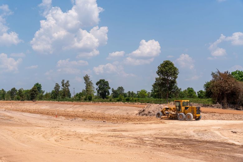 Yellow bulldozer grading a sandy construction site under a blue sky with trees in the background