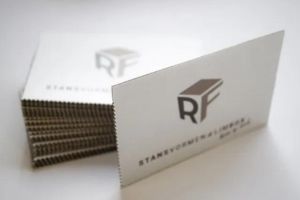 Een stapel witte visitekaartjes met een zilverkleurig logo, in een goed verlichte omgeving.