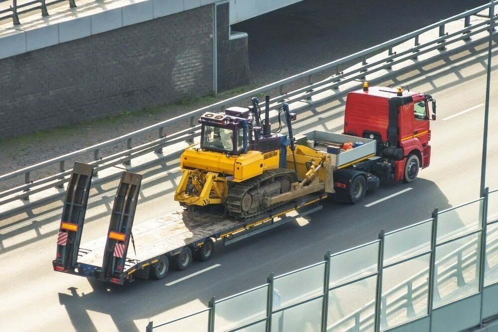 A Red Truck Is Carrying A Yellow Bulldozer On A Trailer On A Highway — RJN Transport In Tamworth, NSW