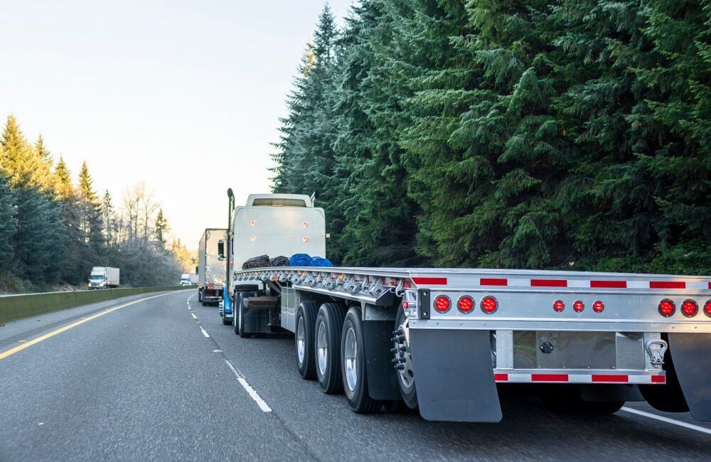 A Semi Truck Is Driving Down A Highway Next To A Forest — RJN Transport In Narrabri, NSW