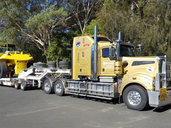A Yellow Semi Truck Is Carrying A Yellow Bulldozer On A Trailer — RJN Transport In Glen Innes, NSW
