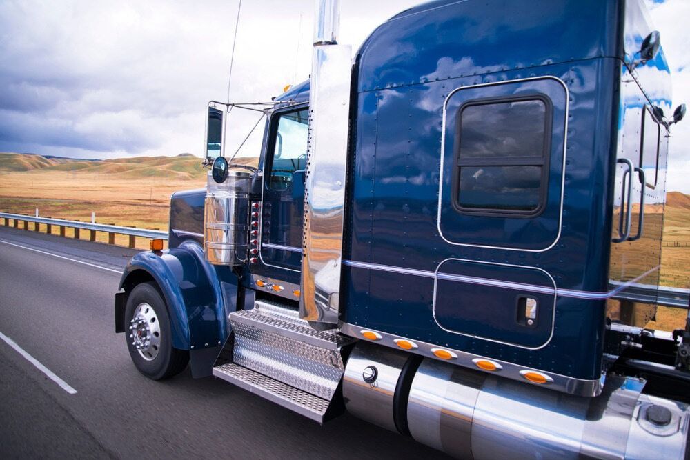 A Blue Semi Truck Is Driving Down A Highway — RJN Transport In Moree, NSW