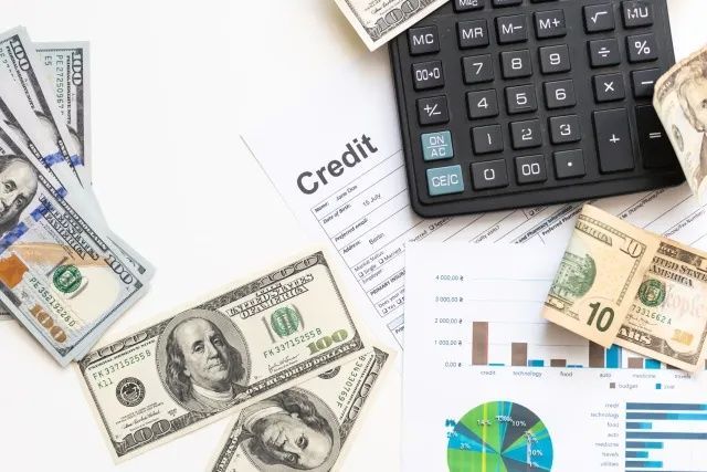 Financial documents, calculator, and U.S. dollar bills on a desk with charts and credit sheet