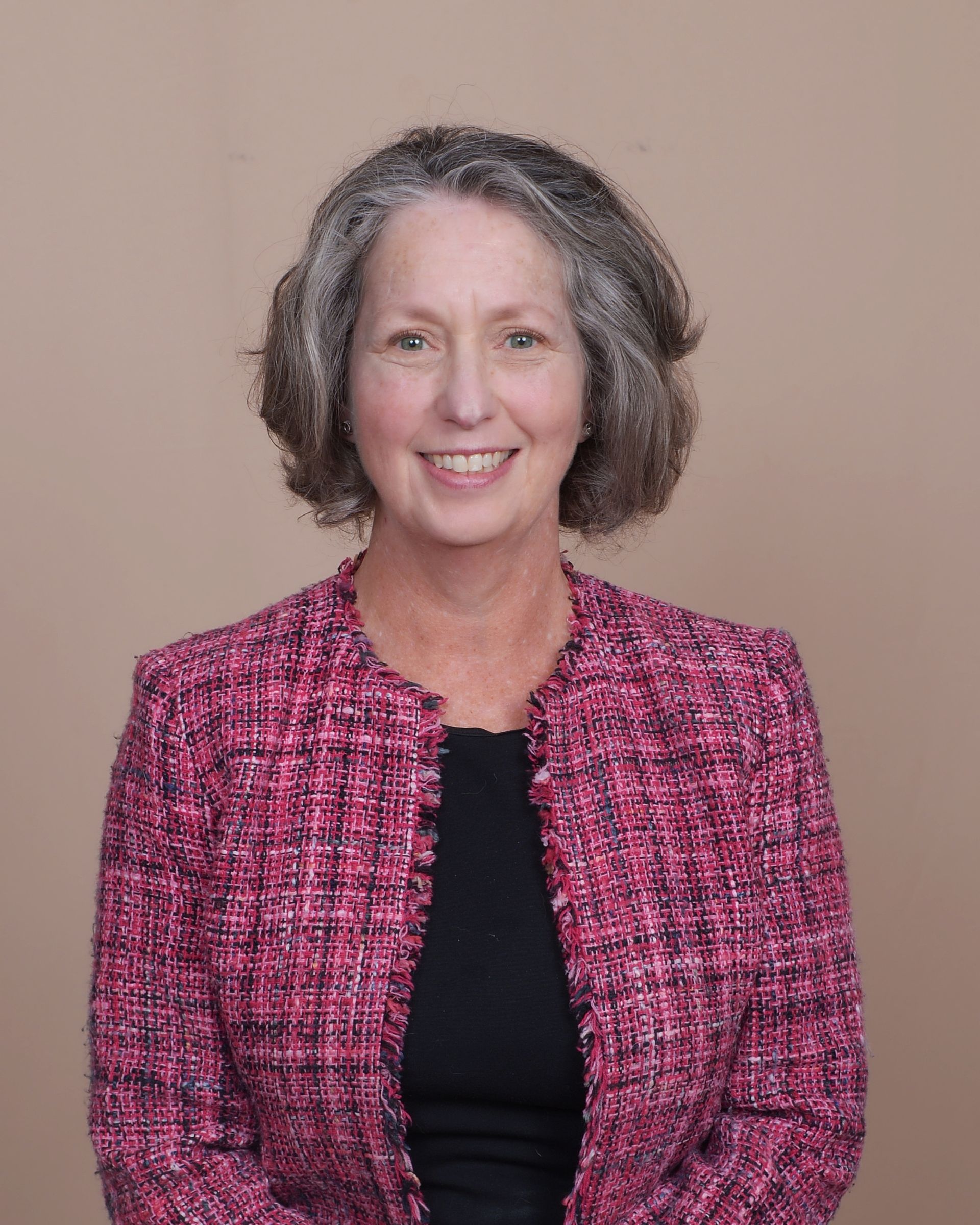 Smiling person in a pink tweed jacket over a black top against a plain beige background