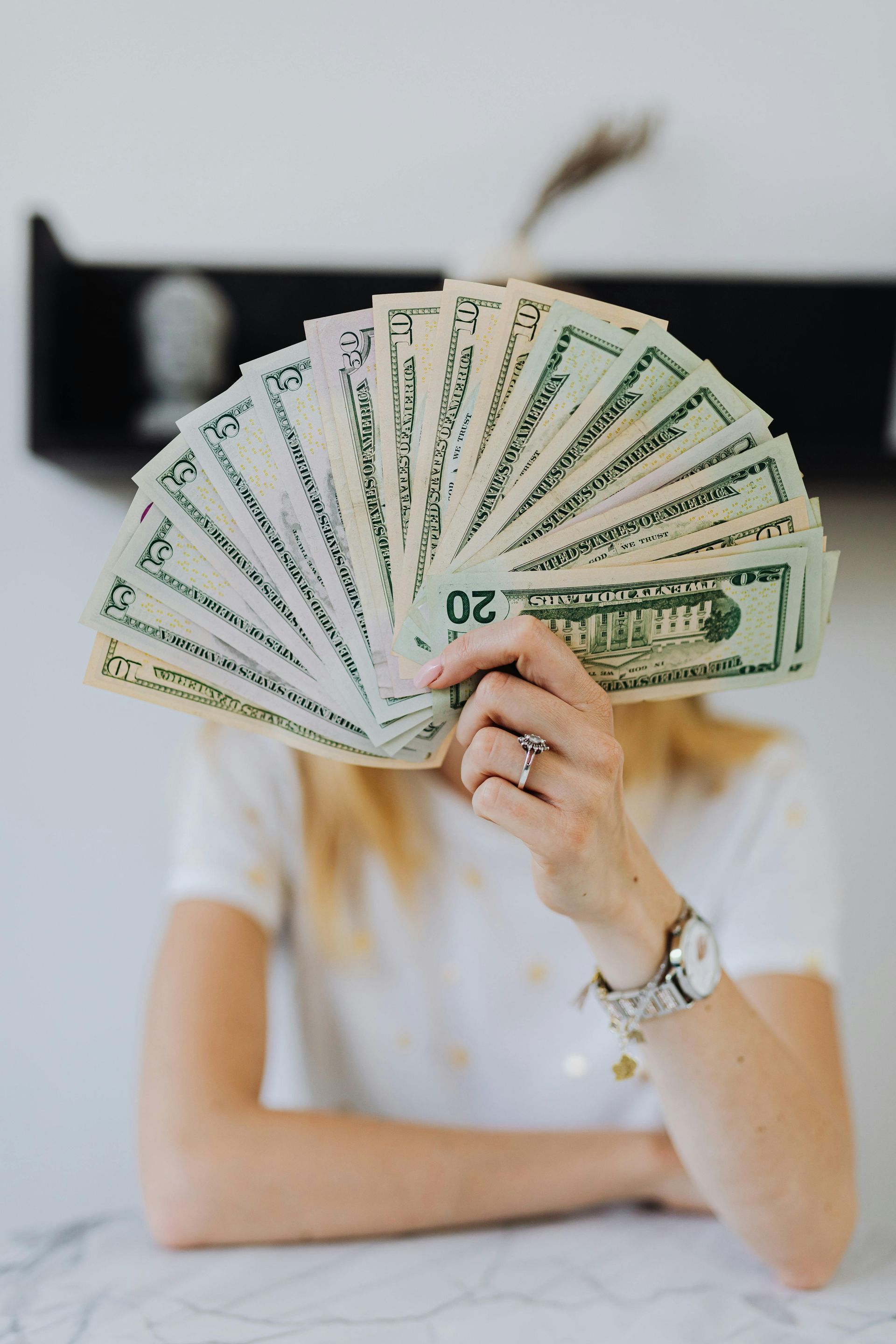 A woman is holding a fan of money in front of her face.