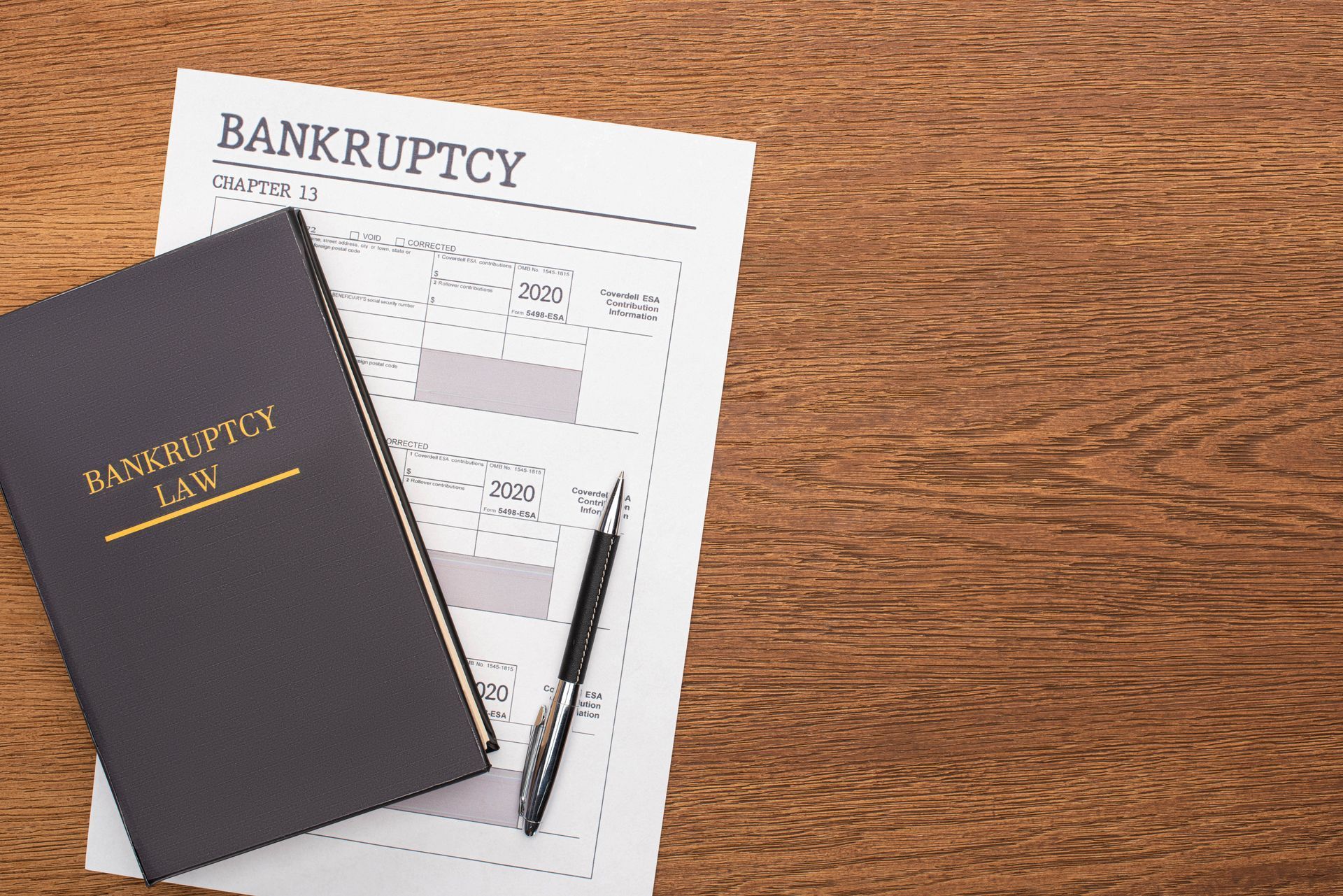 A book titled bankruptcy law is sitting on a wooden table next to a pen.