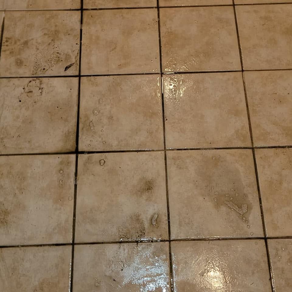 Wet beige tiled floor with dark grout lines and scattered dirt stains.