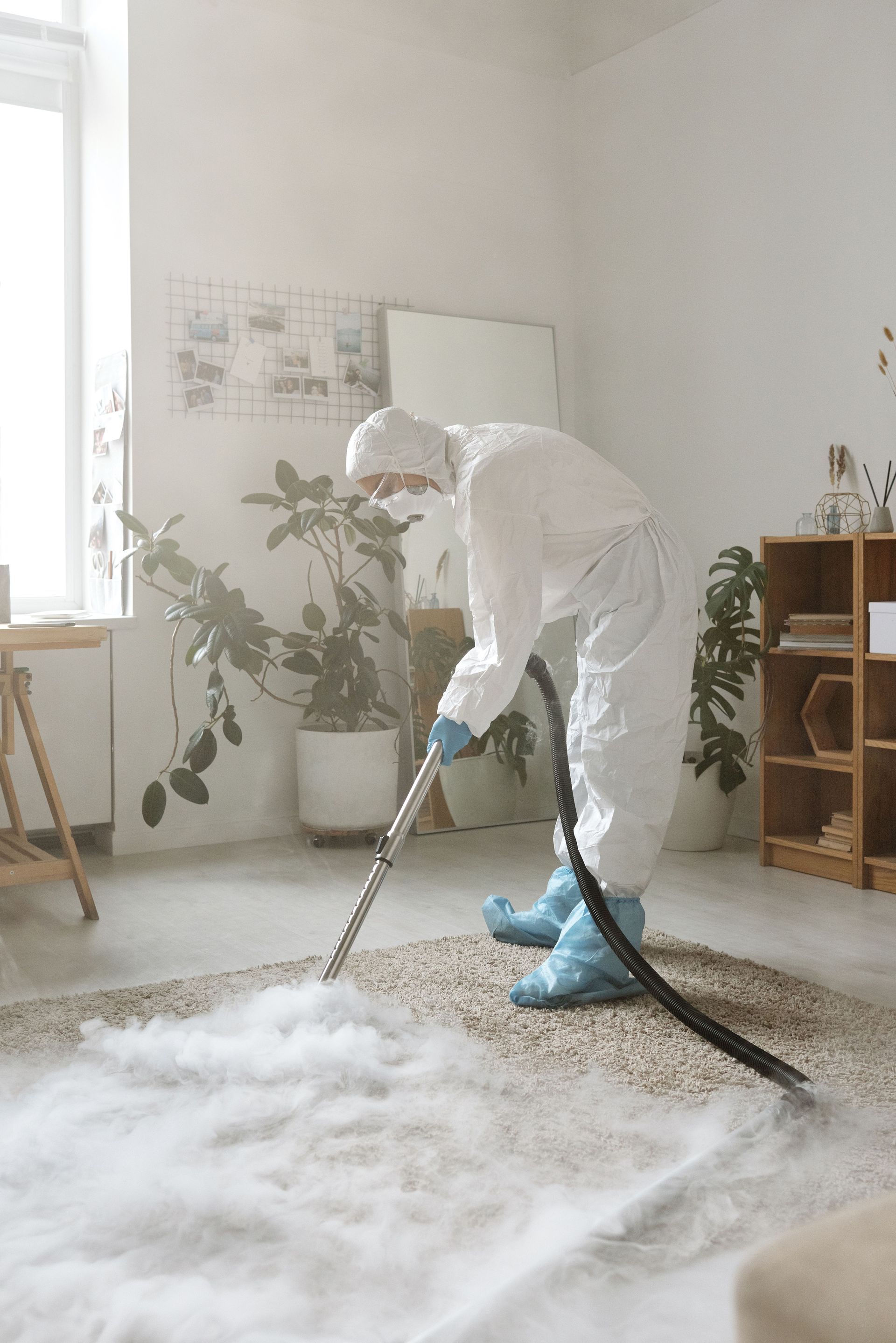 Person in protective gear vacuuming a large white shag rug in a bright room
