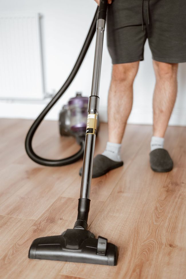 Person vacuuming a hardwood floor with a canister vacuum and black hose