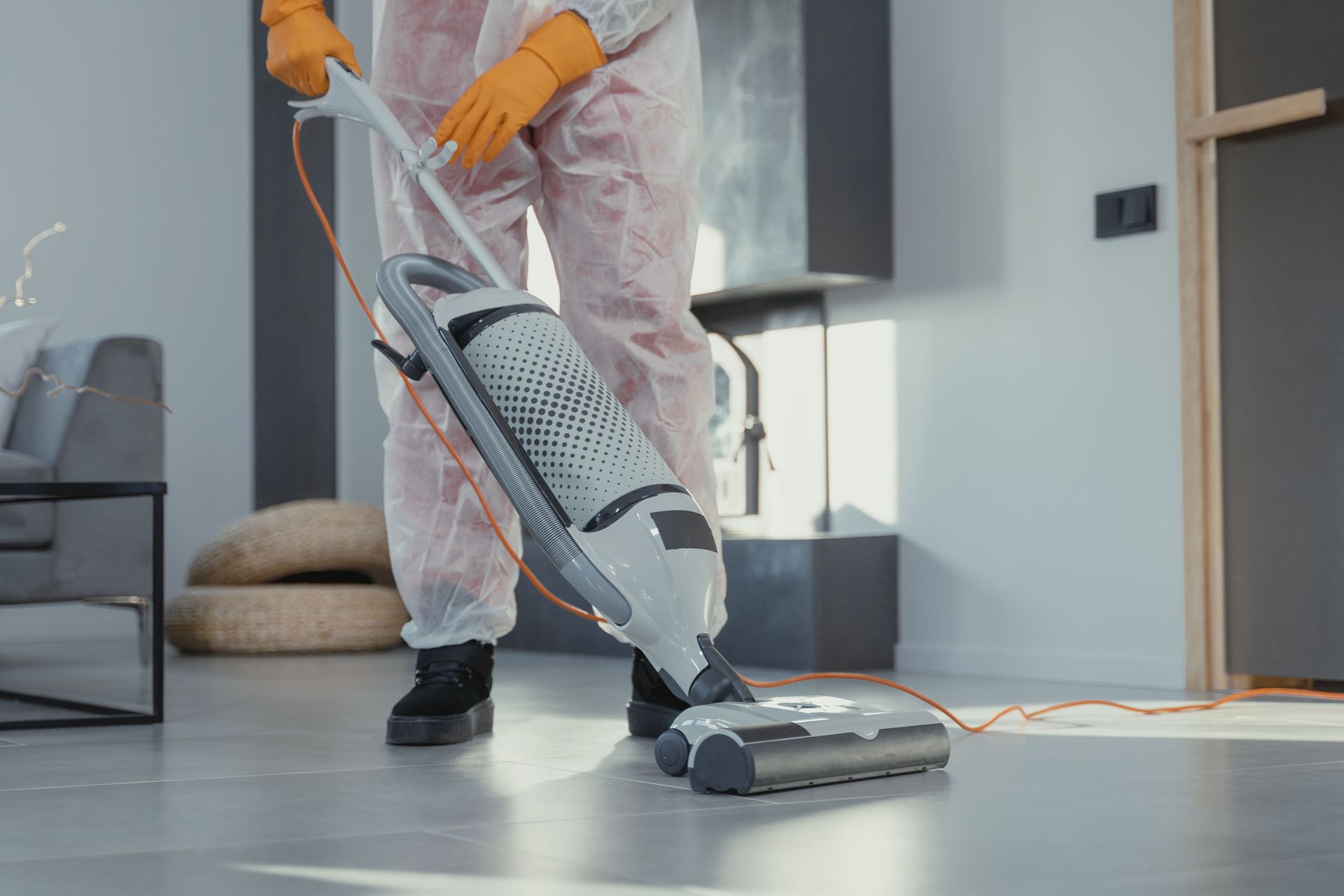 Person vacuuming a light-colored floor in a modern living room with a canister vacuum.