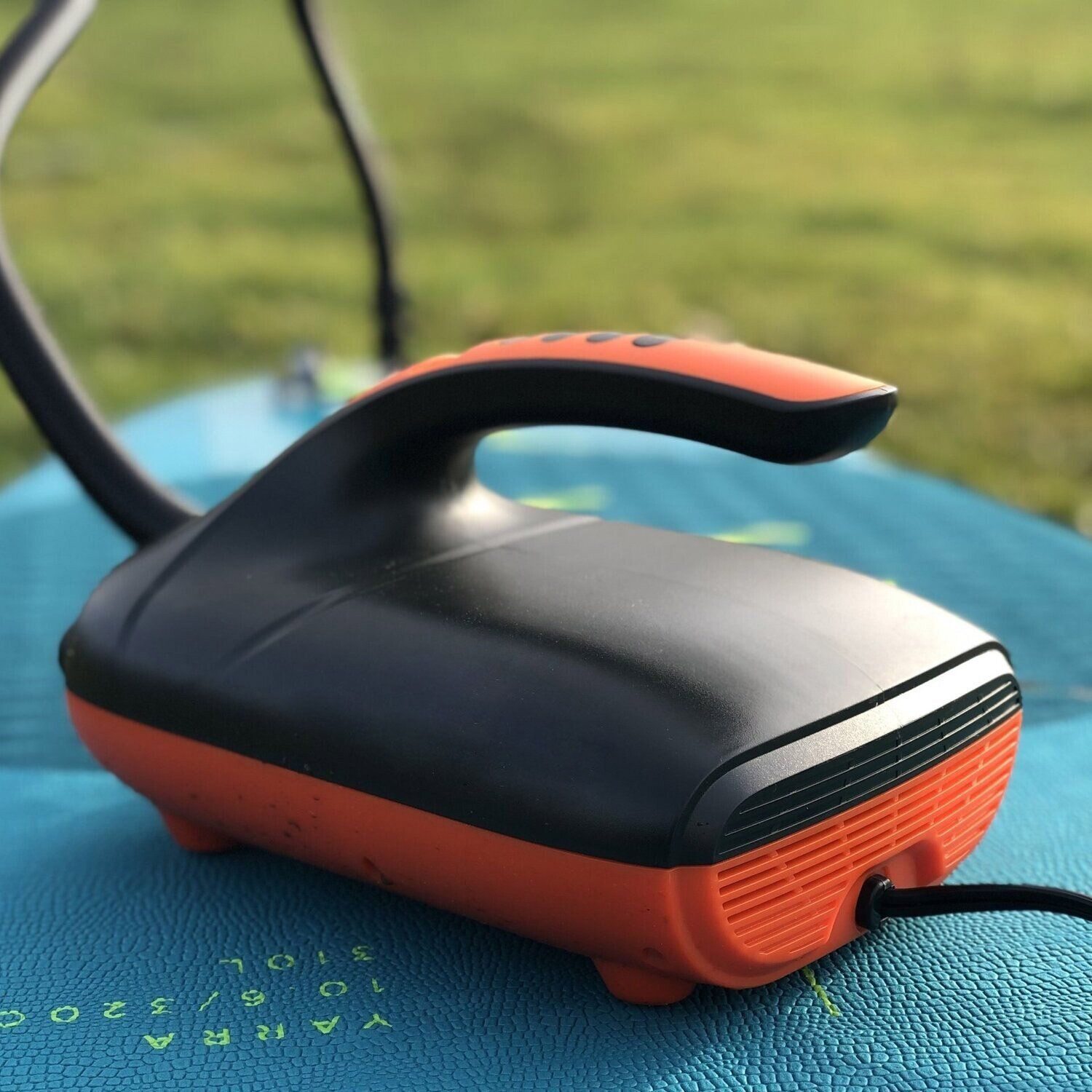 Een oranje en zwarte elektrische luchtpomp staat buiten op een blauw opblaasbaar oppervlak.