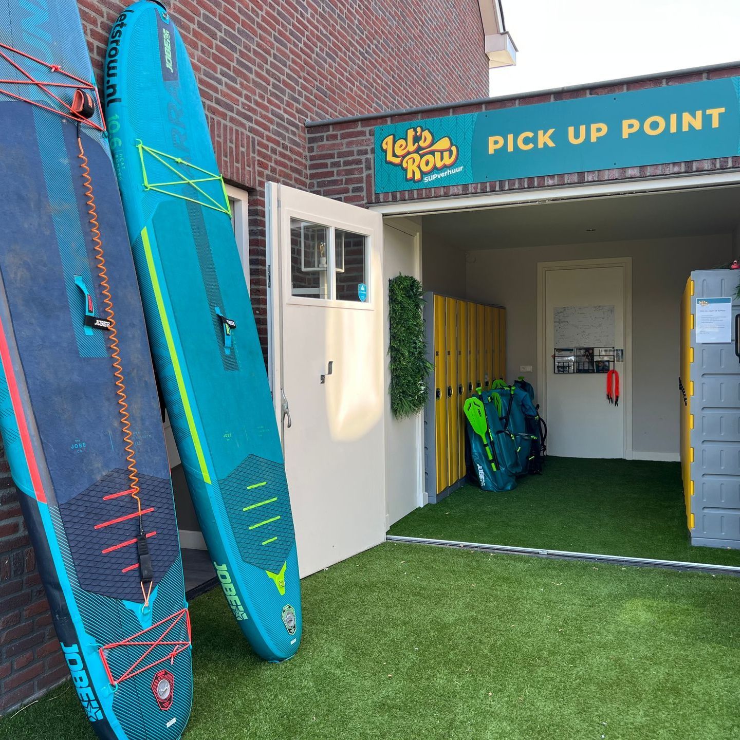 Twee stand-up paddleboards staan ​​tegen een bakstenen muur buiten een ophaalpunt van 