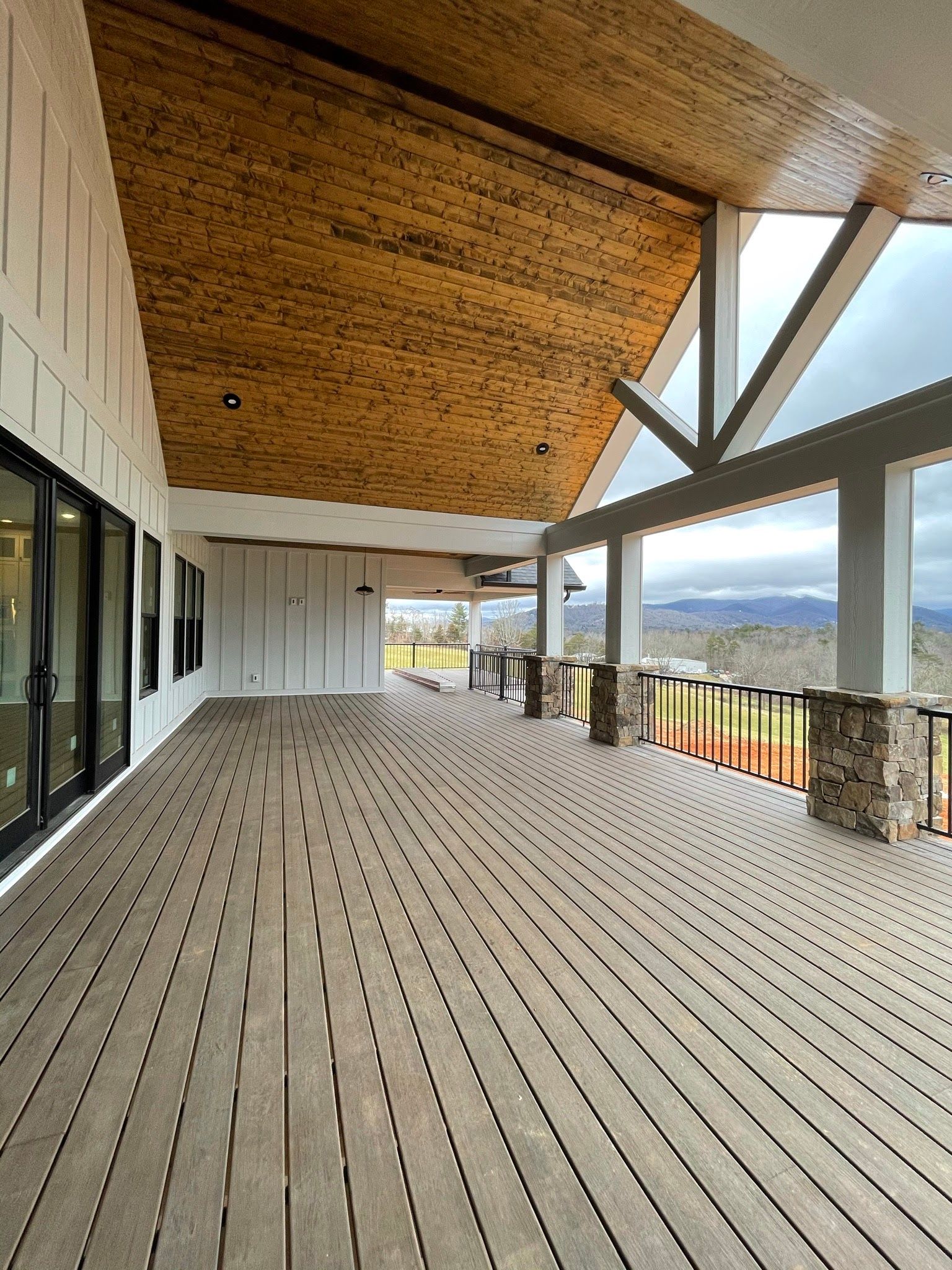A large empty deck with a wooden ceiling and sliding glass doors.