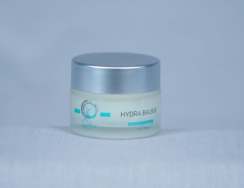 Small jar of Hydra Baume skincare product, silver lid, blue text, on white cloth.