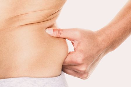 A hand pinching a roll of skin on a person's side, showing body fat.