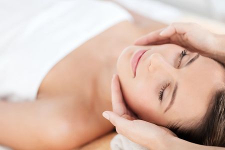 Woman receiving facial massage, eyes closed, hands on her face.