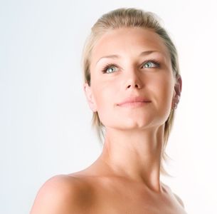Blond woman with blue eyes, looking upwards with a slight smile, bare shoulders, soft lighting.