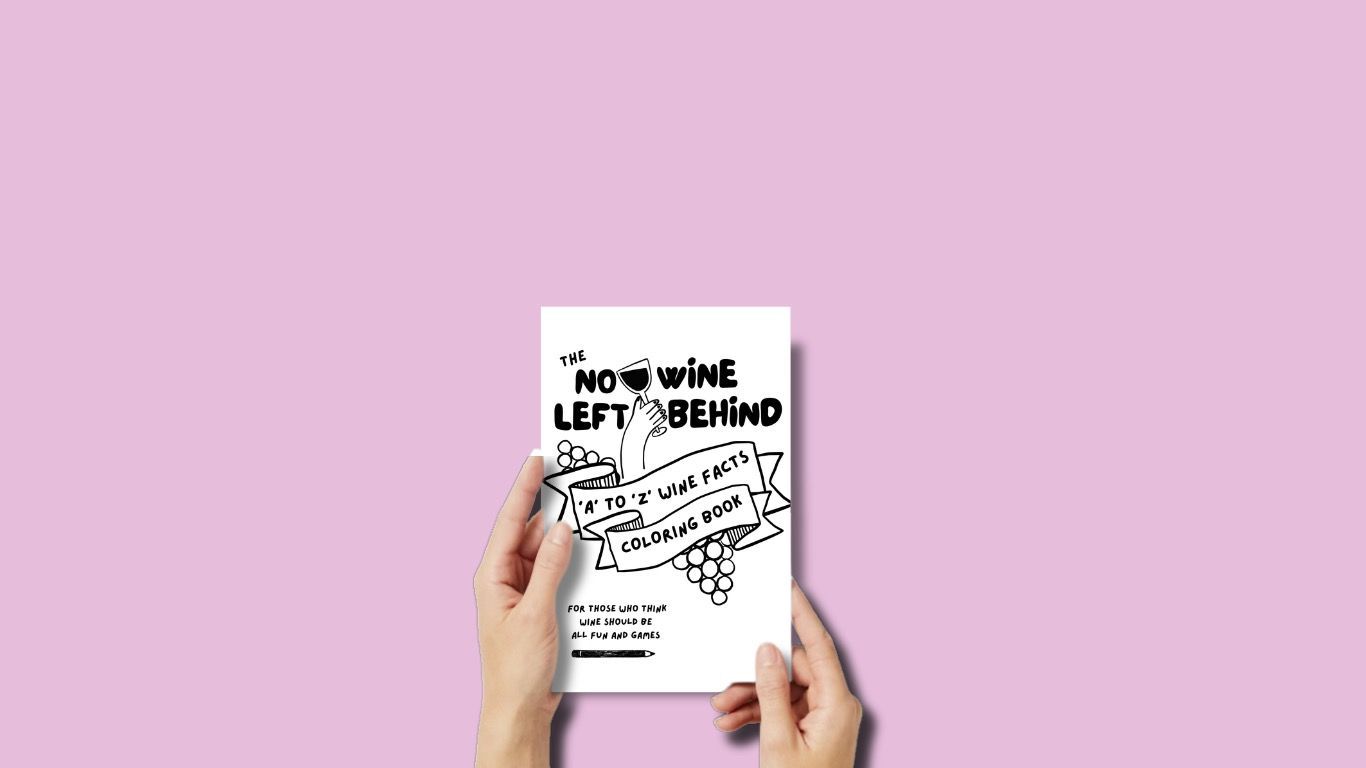 Two hands holding No Wine Left Behind’s interactive wine coloring book with a white cover and black design, titled “A to Z Wine Facts Coloring Book.”