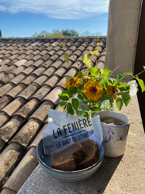 Rooftop scene with slices of bread in a bowl, French bakery packaging, a mug of tea, and a vase of yellow flowers