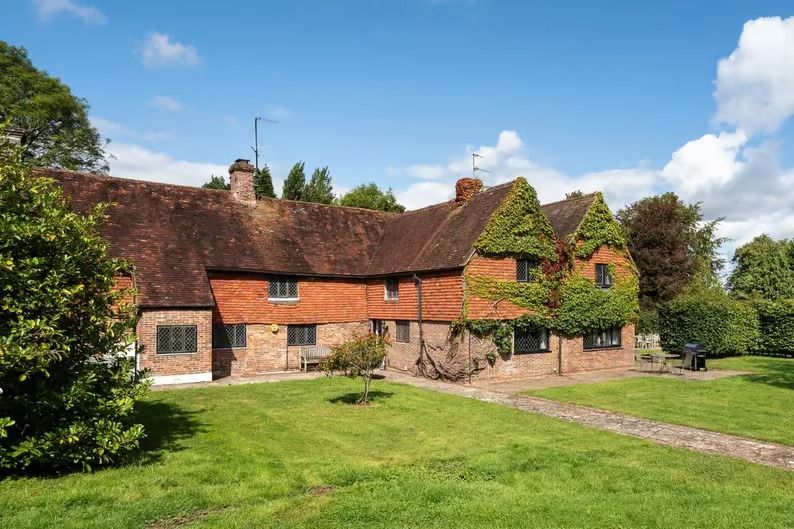 Rustic cottage with red-tiled roof and brick walls on a grassy lawn under a blue sky