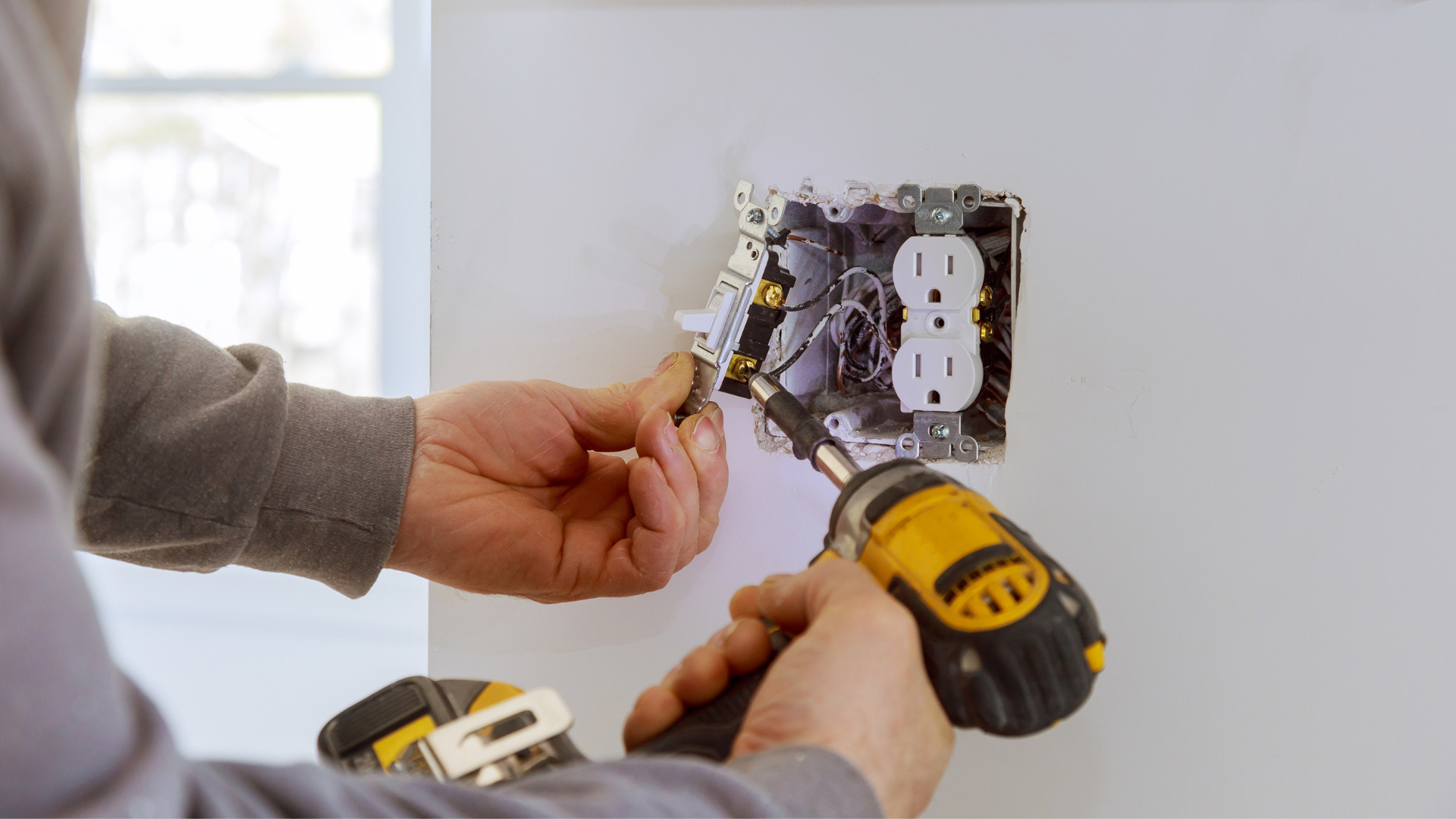 Hands installing an electrical outlet with a drill during home repair