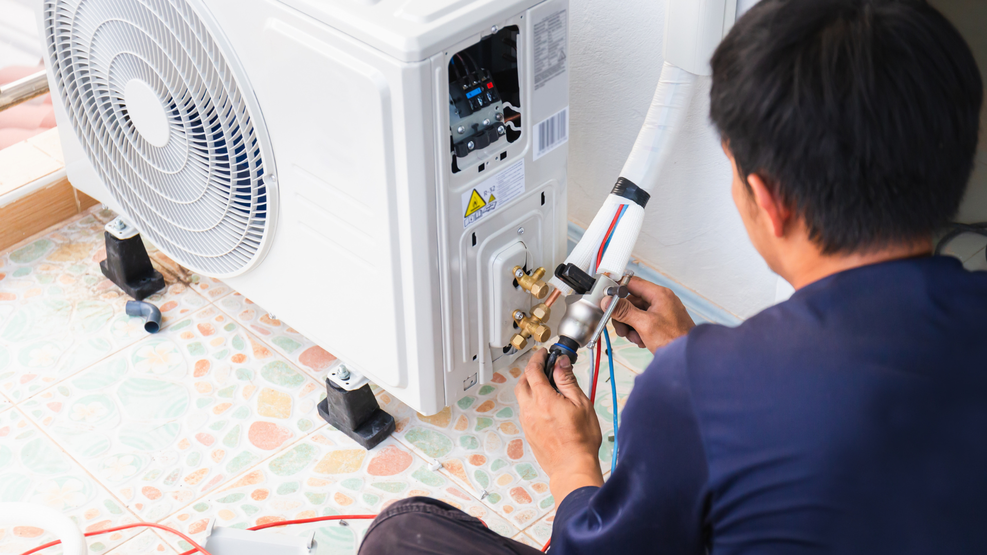 Technician repairing the back of a white air conditioner unit with tools on a patterned floor