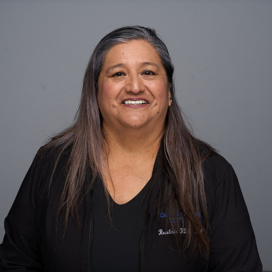 Smiling person with long dark hair in a black shirt against a gray background