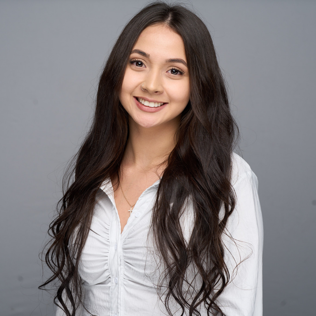 Smiling woman with long dark hair in a white blouse against a gray background