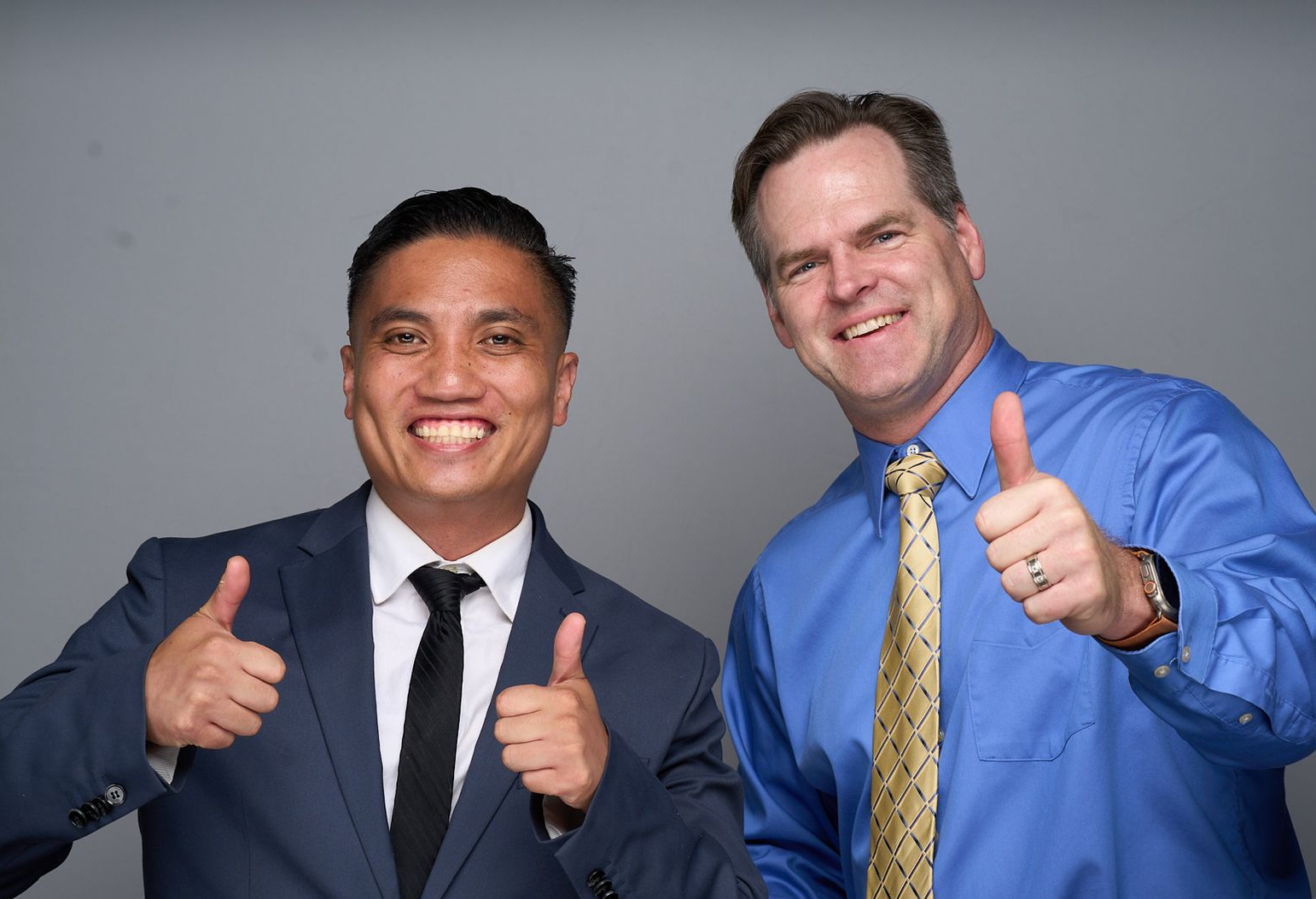 Two smiling staff members in black shirts stand with arms crossed in a bright office reception area.