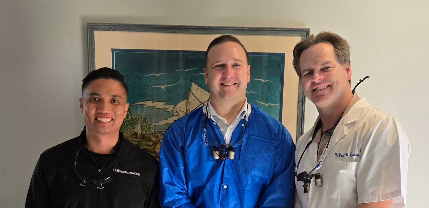 Three men standing together indoors, smiling in front of framed wall art.