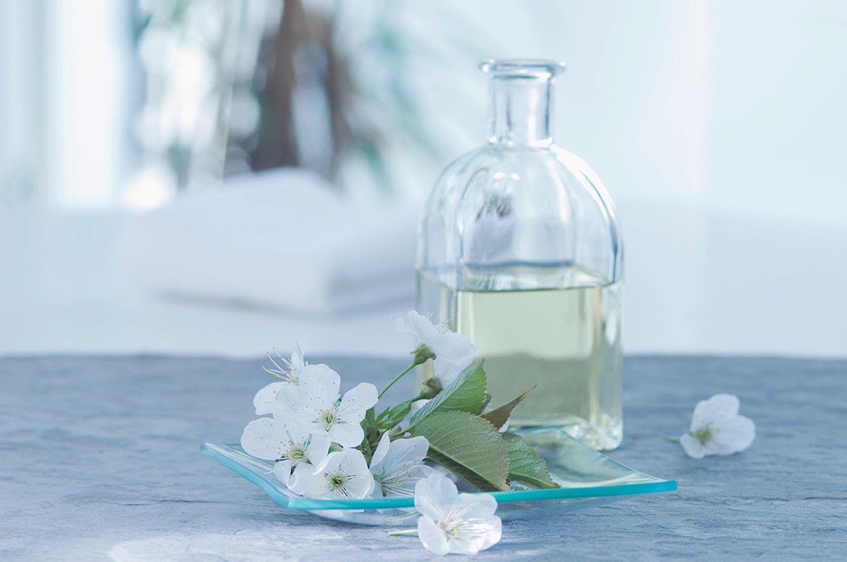 Glass bottle with pale green liquid and white flowers on a blue surface