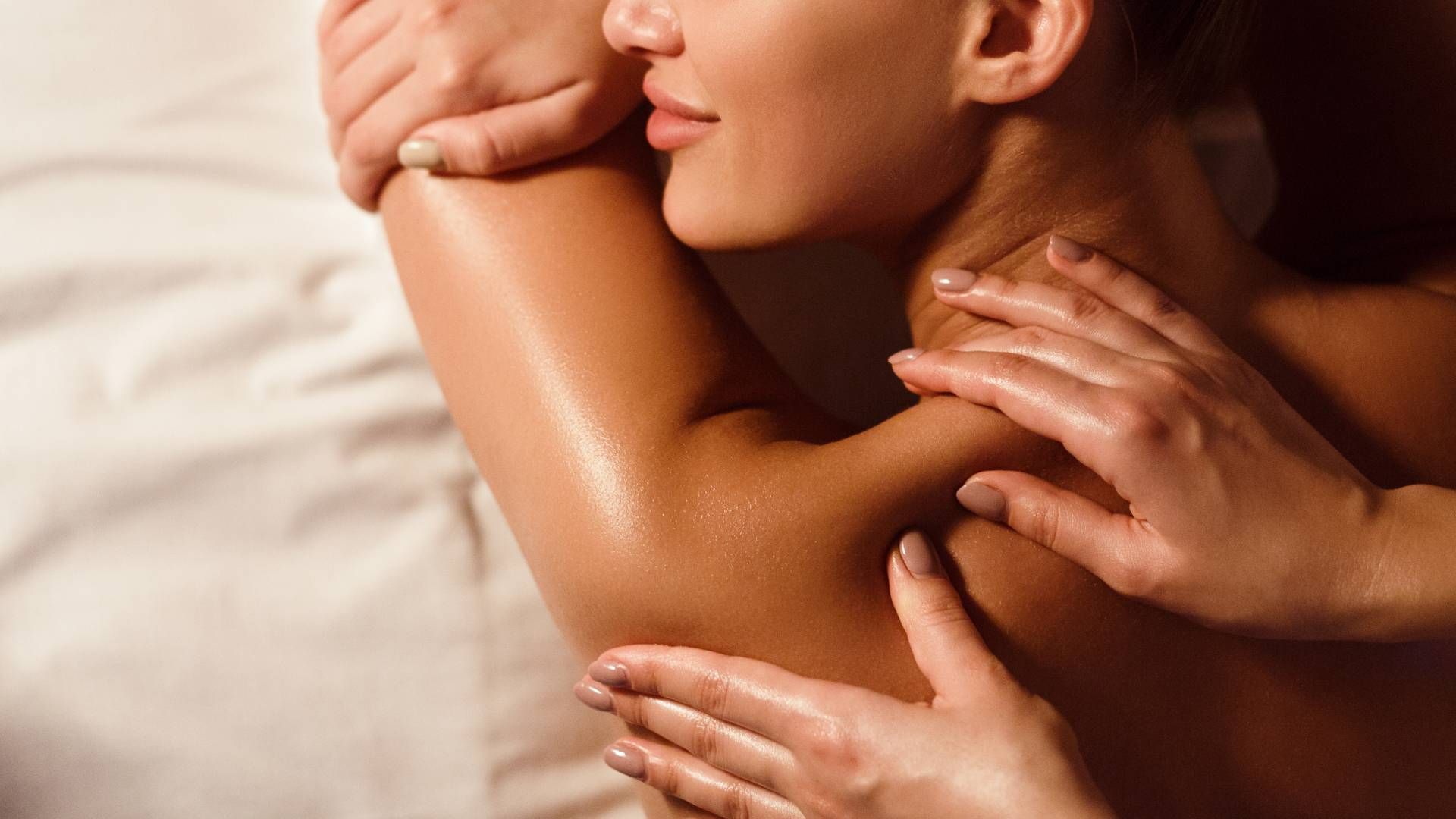 Close-up of a person receiving a back massage with oil on a soft beige bed.
